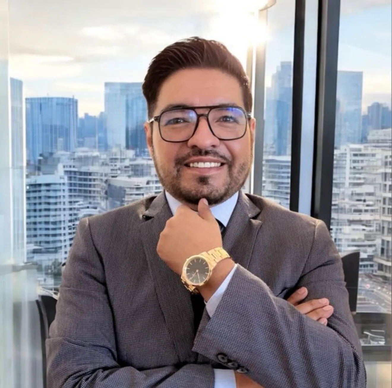 Retrato de Carlos Pimentel: hombre con lentes, barba y traje gris, sonriendo frente a una ventana